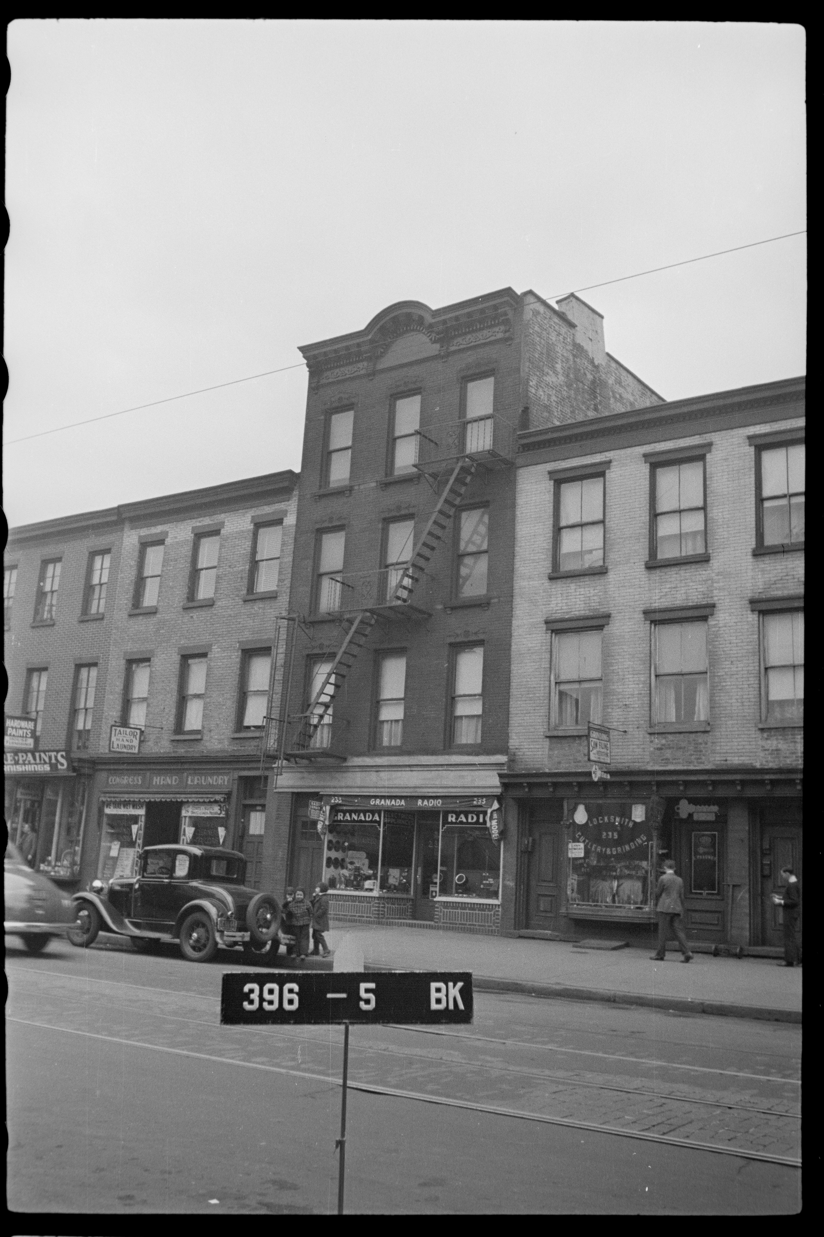 1940s tax photograph of the Granada Radio storefront at 233 Court Street, Brooklyn, with a locksmith next door and a vintage car parked out front.